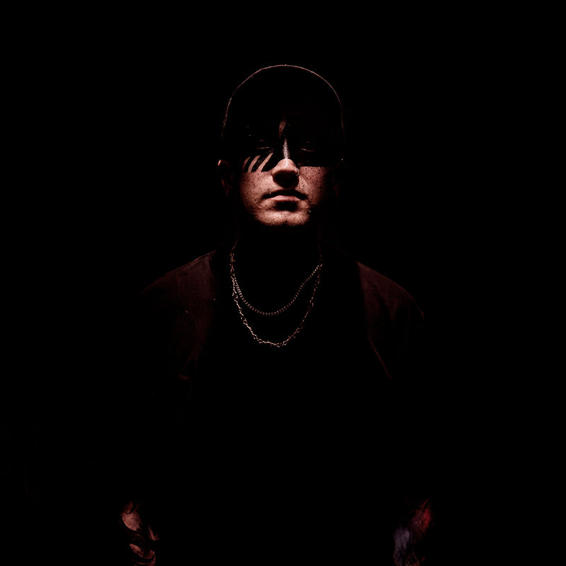 Person wearing a cap and chain necklace in a dark setting