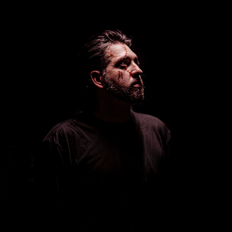 Man with a beard and dark clothing against a black background