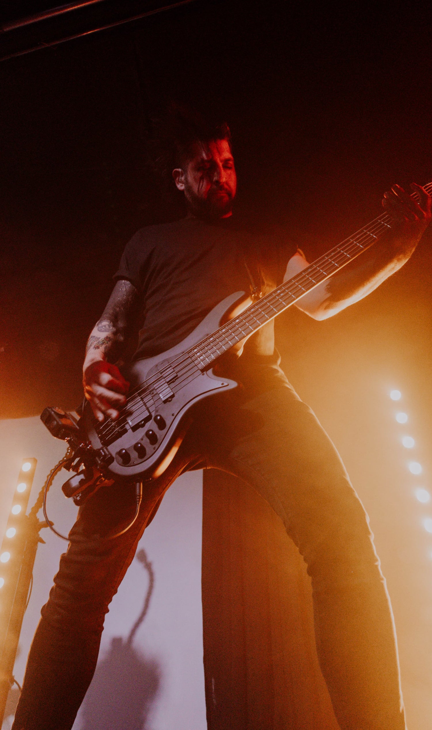 Christain Kwitowski playing bass guitar on stage with red lighting for the band Stories Through Storms